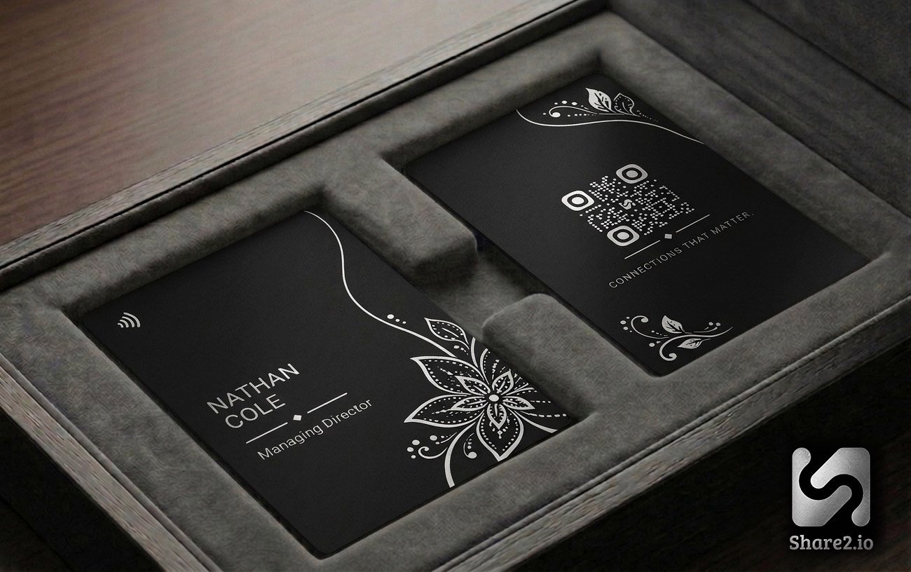 Bloom design — matte black NFC business card with an intricate gold botanical flower pattern and engraved QR code, presented in a grey suede gift box